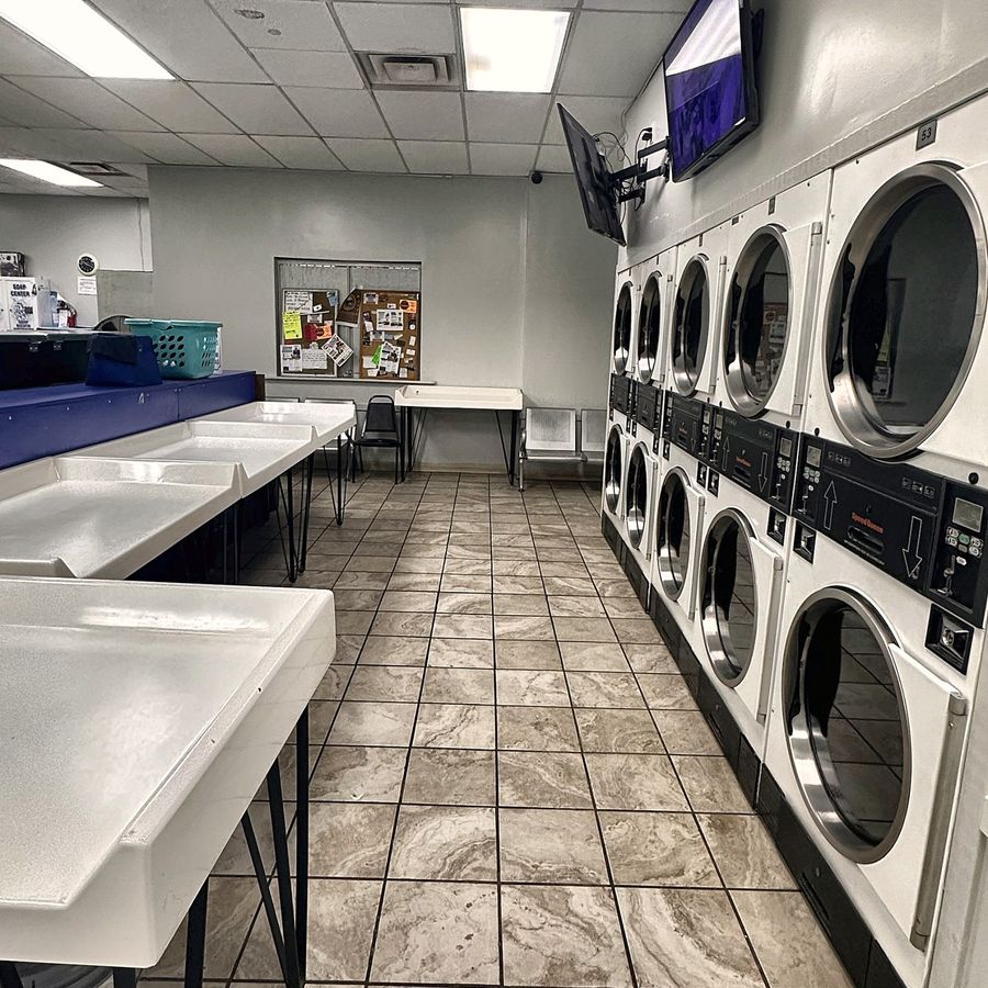 Long white folding counters facing a row of dryers, with a wall-mounted TV above